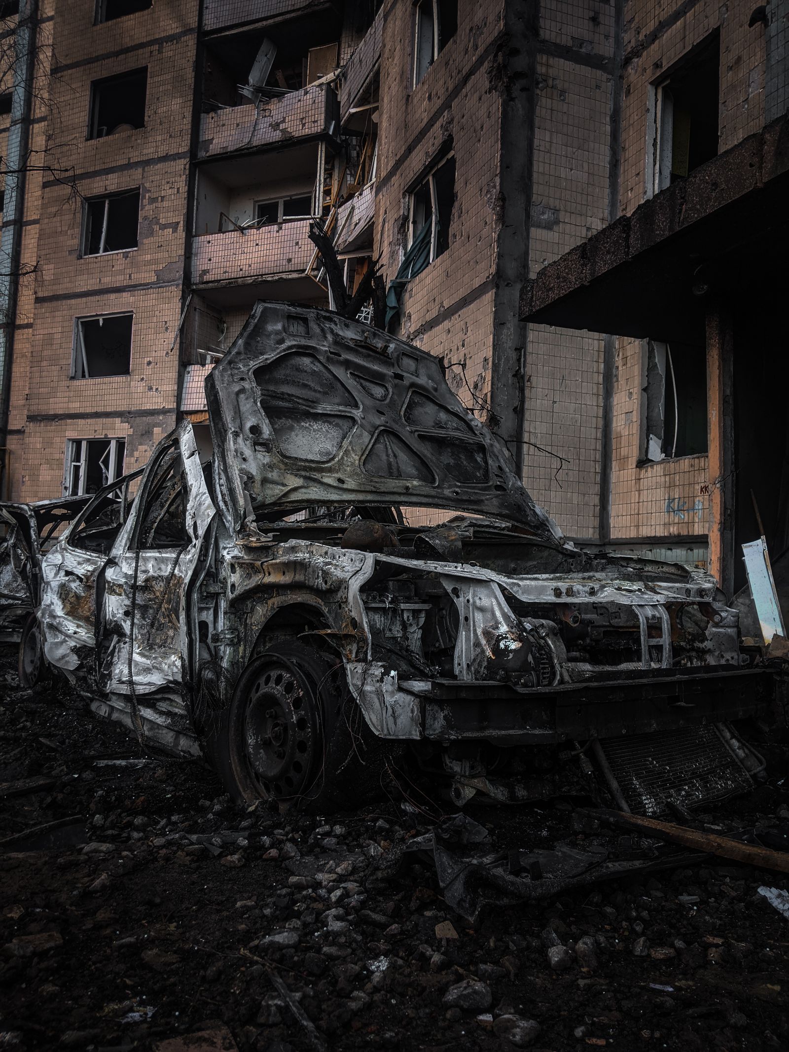 A burned-out car in front of a shelled apartment building