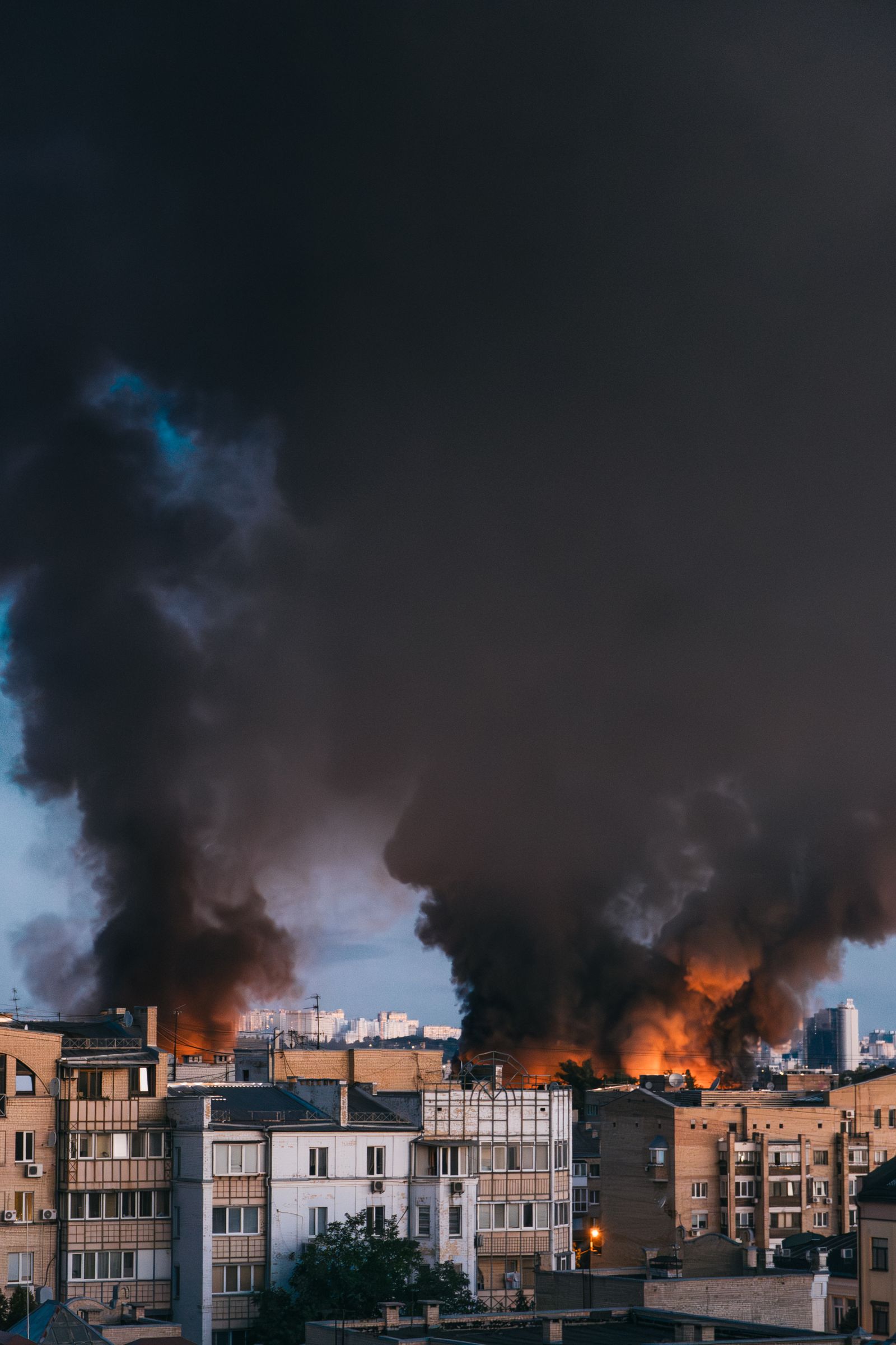 Columns of black smoke rising over a city skyline at dusk