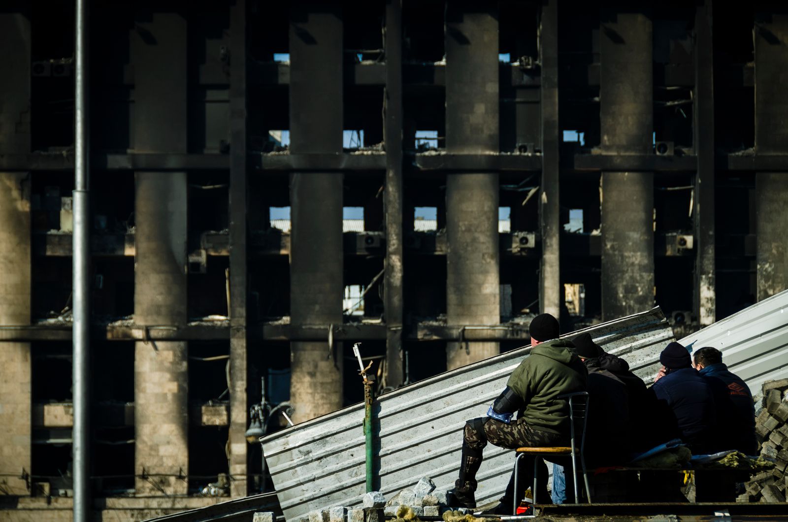 People sitting on debris in front of a burned-out building