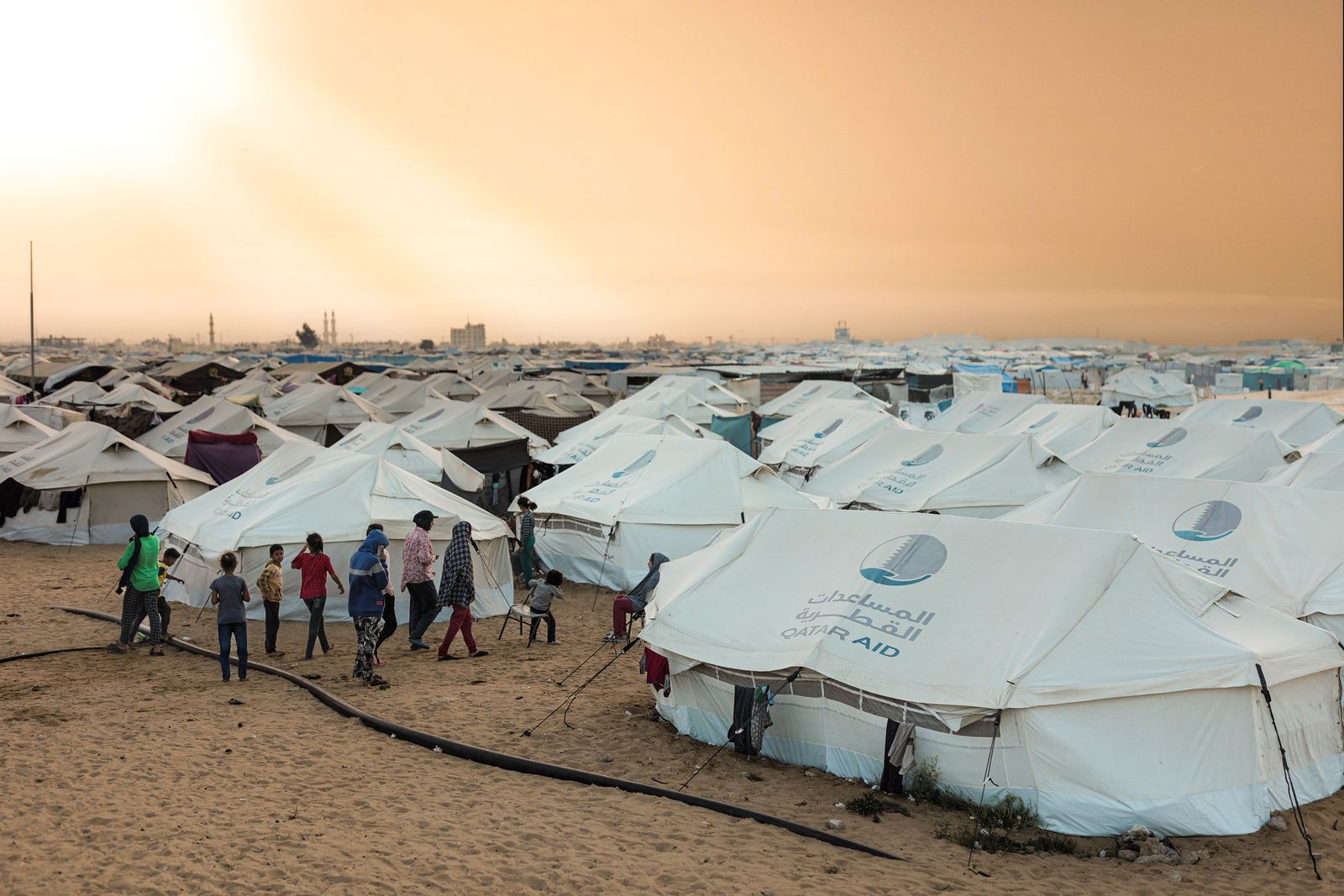 Children walking between aid tents in a displacement camp at dusk