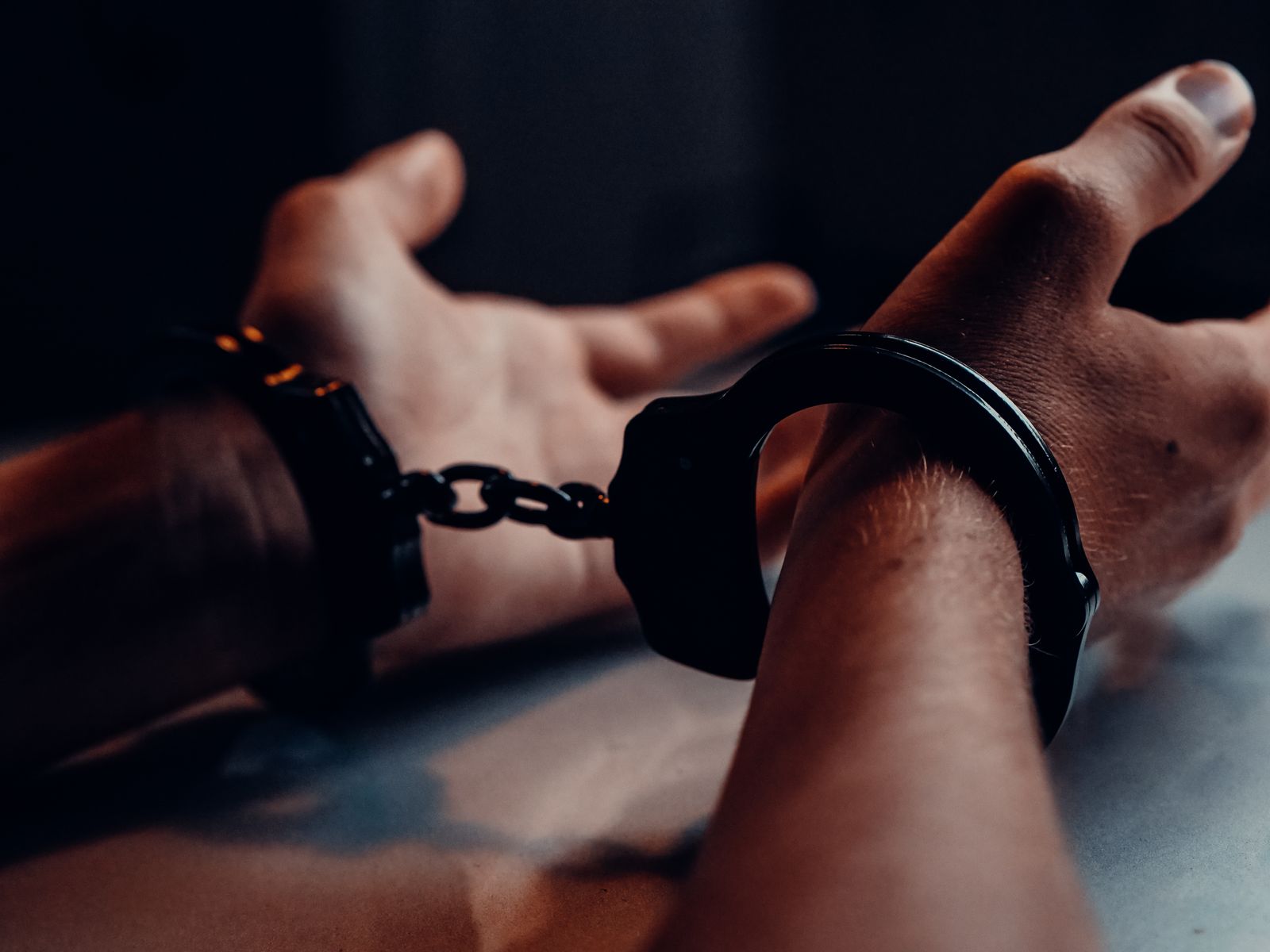 Handcuffed hands resting on a table in a dark room