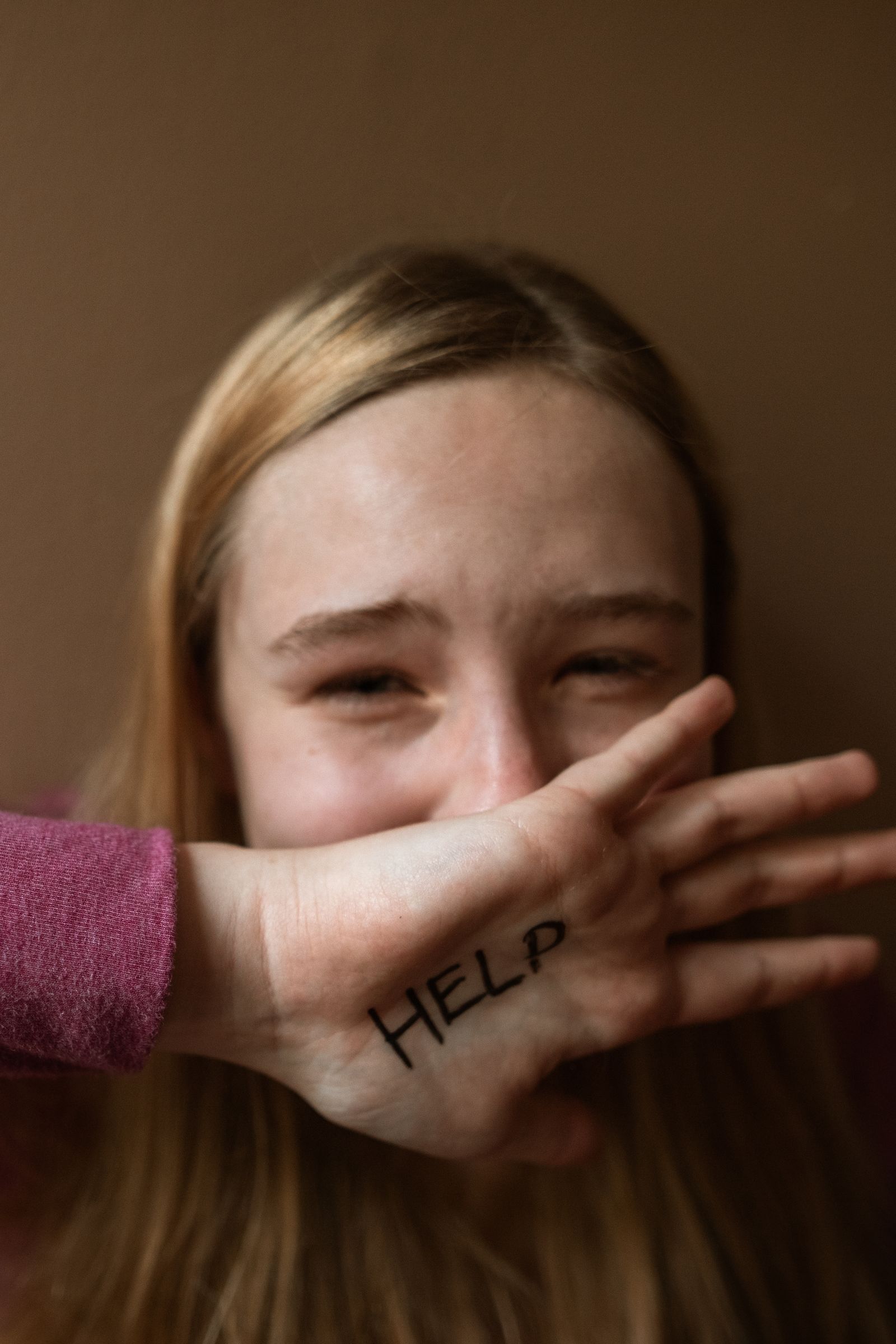 A girl covering her mouth with a hand marked HELP
