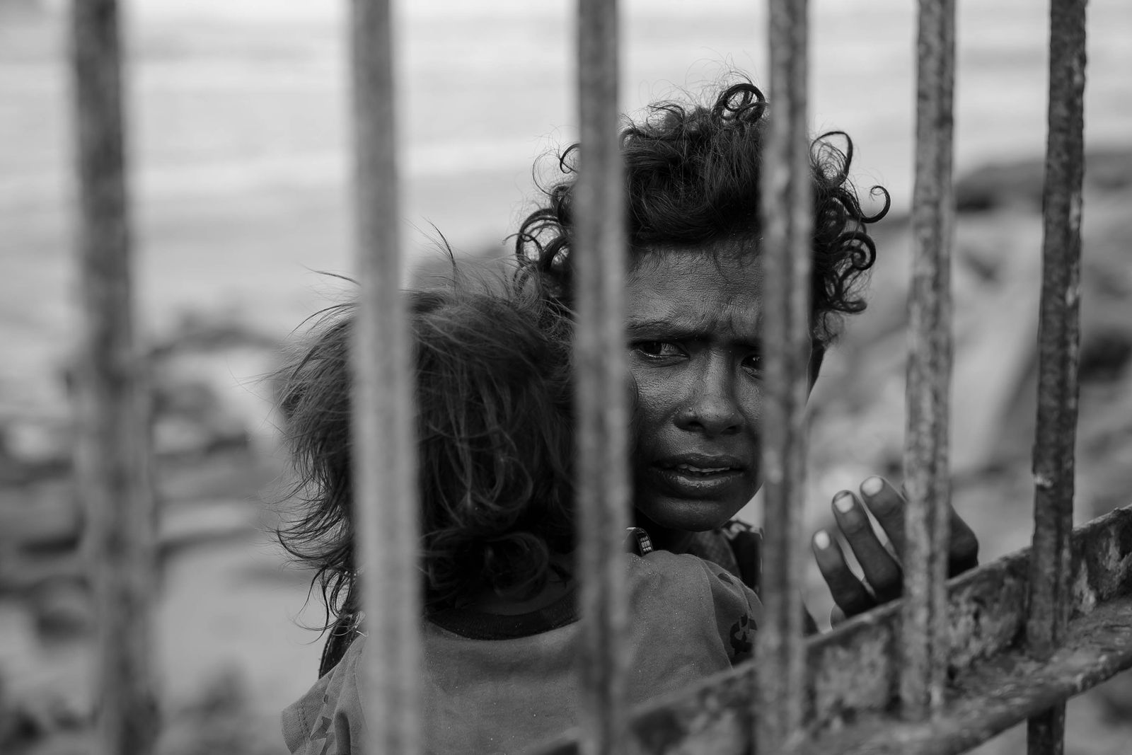 A mother holding her child, looking out from behind iron bars