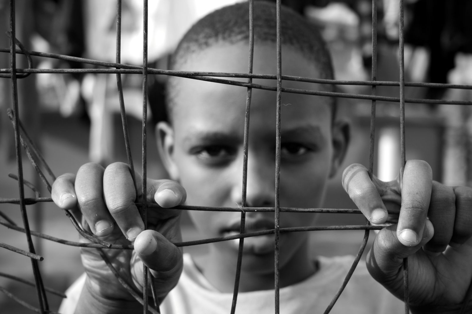 A boy gripping a wire fence, looking directly at the camera