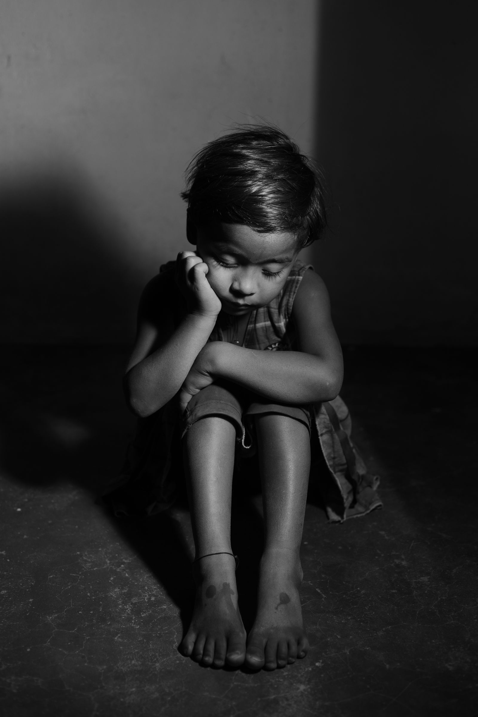 A child sitting alone against a wall in low light