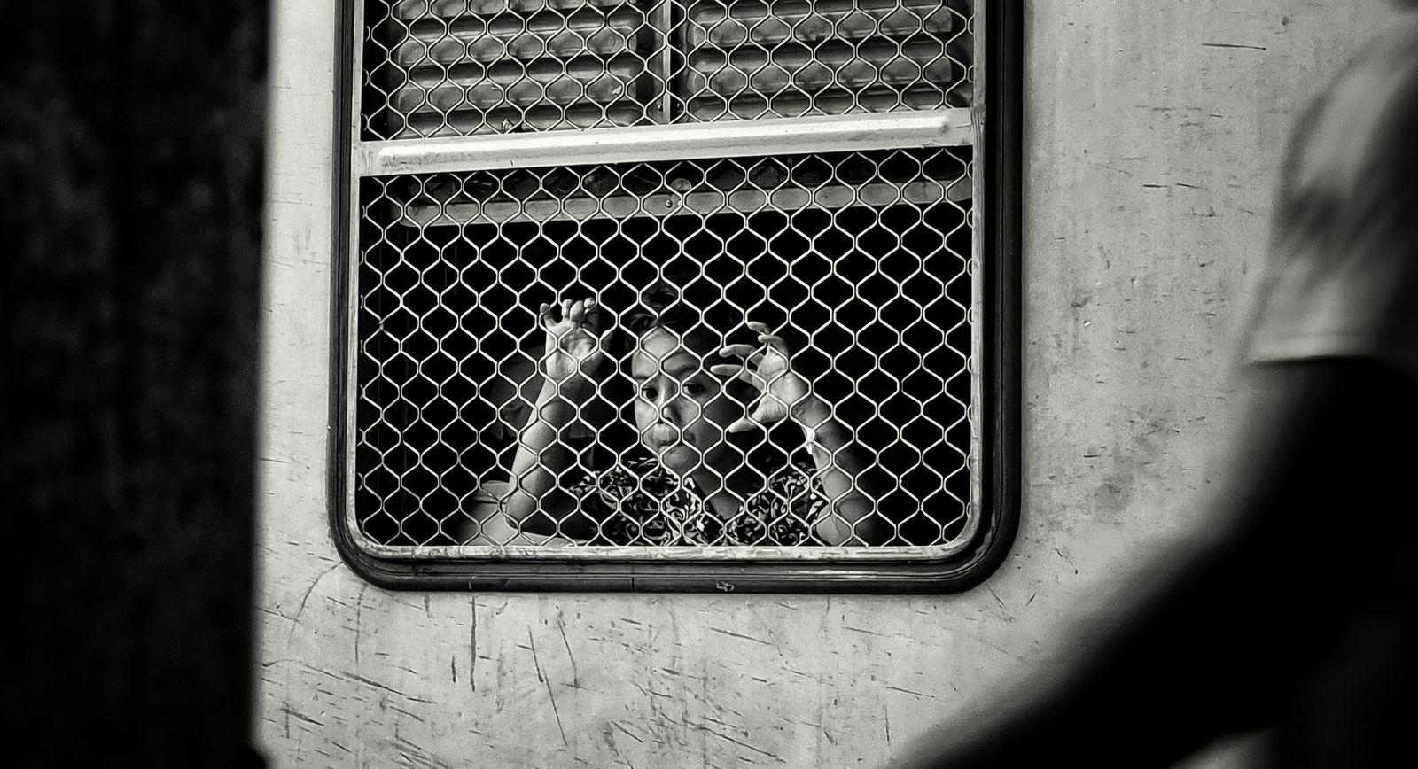 A child looking out through the meshed window of a train car